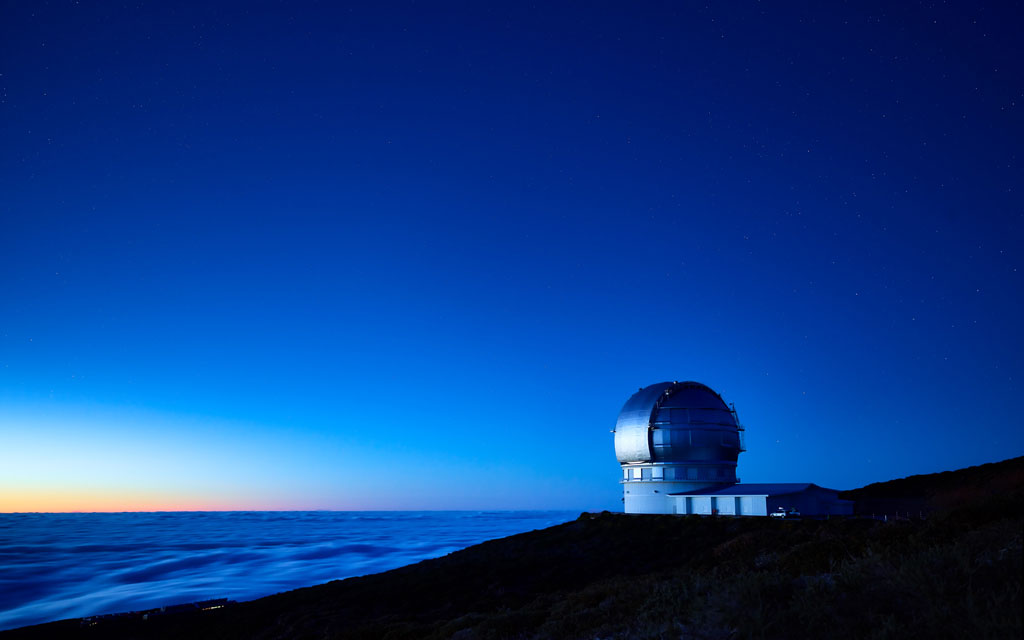 Blick auf ein Observatorium unter den Sternen und über der Wolkendecke